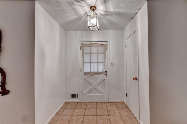 doorway with a textured ceiling and light tile patterned flooring