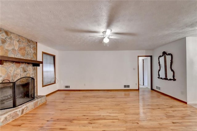 unfurnished living room with ceiling fan, light hardwood / wood-style flooring, a fireplace, and a textured ceiling