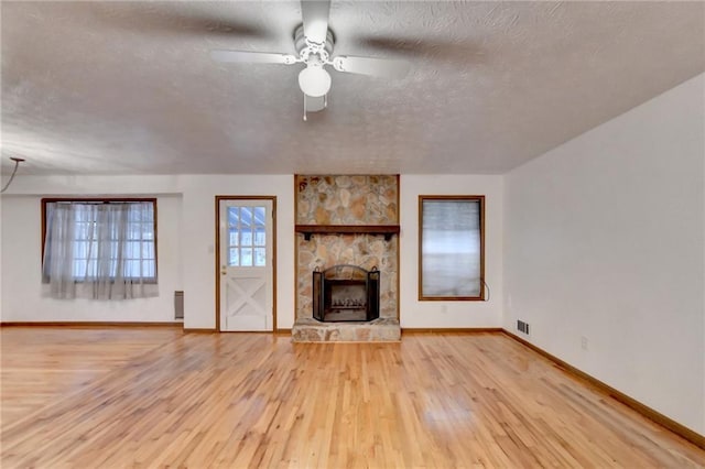 unfurnished living room featuring a textured ceiling, a fireplace, ceiling fan, and light wood-type flooring