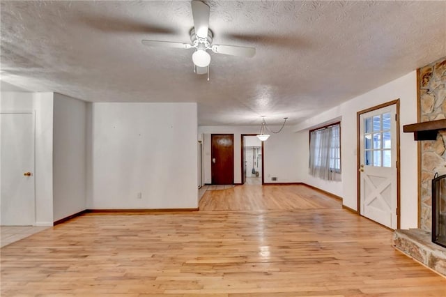 unfurnished living room with ceiling fan, a fireplace, light hardwood / wood-style floors, and a textured ceiling