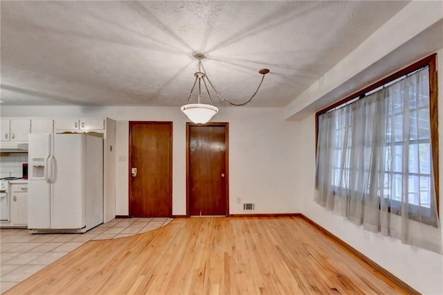 unfurnished dining area with a textured ceiling and light wood-type flooring