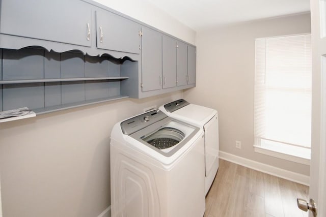 laundry area with light wood-type flooring, washing machine and dryer, cabinet space, and baseboards