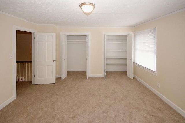 unfurnished bedroom with carpet floors, crown molding, two closets, a textured ceiling, and baseboards