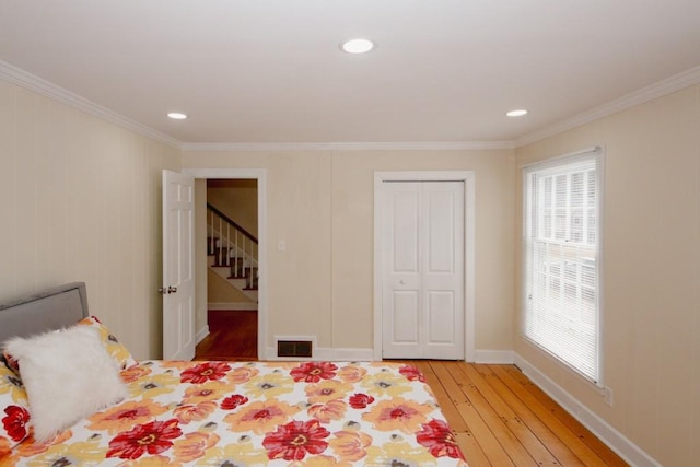 bedroom with baseboards, light wood finished floors, visible vents, and crown molding