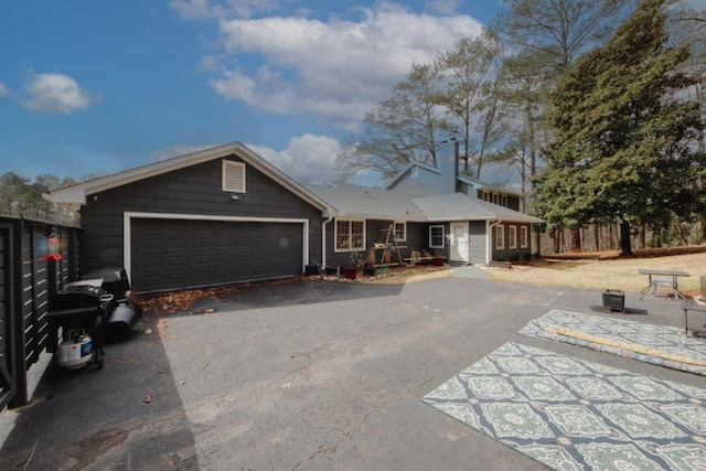 ranch-style home with an attached garage, a chimney, and aphalt driveway