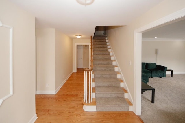 staircase with ornamental molding, baseboards, and wood finished floors