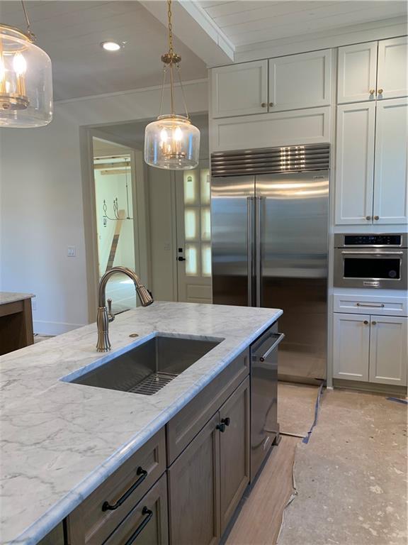 kitchen featuring appliances with stainless steel finishes, white cabinetry, a sink, and light stone counters