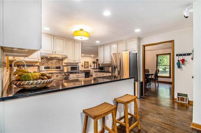 2452 Camp Mitchell Rd, Grayson, GA 30017 - kitchen with stainless steel appliances, under cabinet range hood, a peninsula, dark countertops, and backsplash