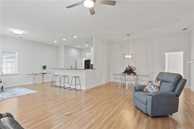 living area with ceiling fan with notable chandelier and light hardwood / wood-style floors