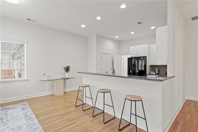 kitchen with white cabinets, dark stone counters, a kitchen breakfast bar, black fridge, and kitchen peninsula