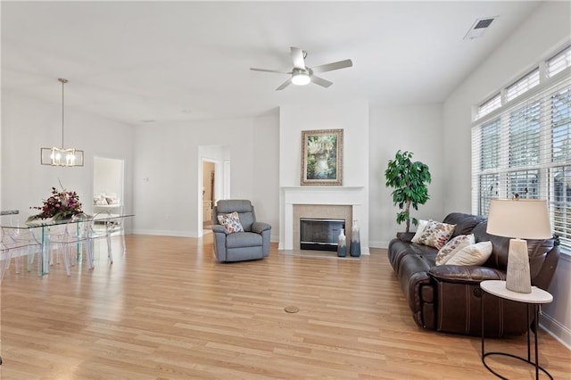 living room with light wood-type flooring, ceiling fan with notable chandelier, and a tile fireplace