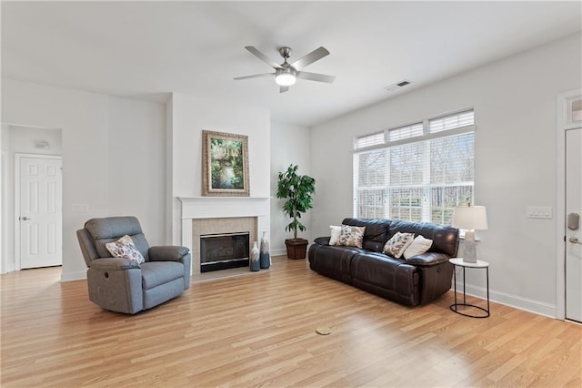 living room with ceiling fan, a tile fireplace, and light hardwood / wood-style flooring