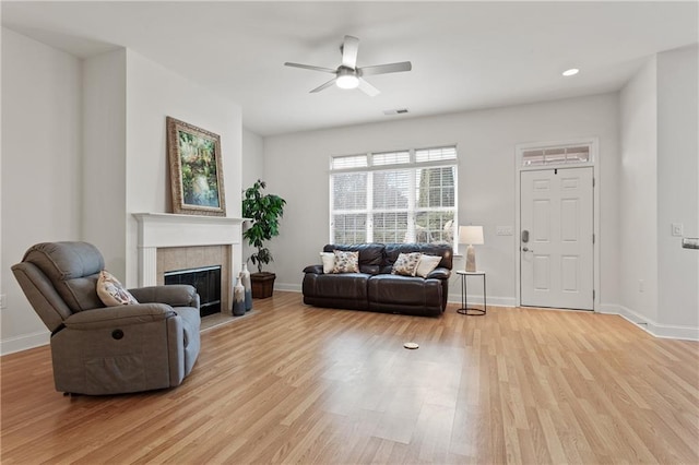 living room featuring ceiling fan, light wood-type flooring, and a tile fireplace