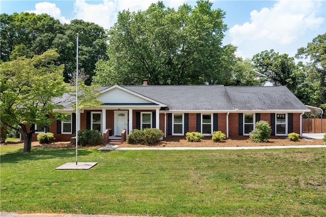 view of front facade featuring roof with shingles, fence, brick siding, a front yard, and covered porch