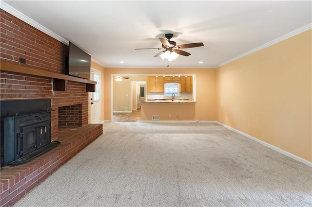 unfurnished living room with ceiling fan, light colored carpet, a wood stove, baseboards, and ornamental molding