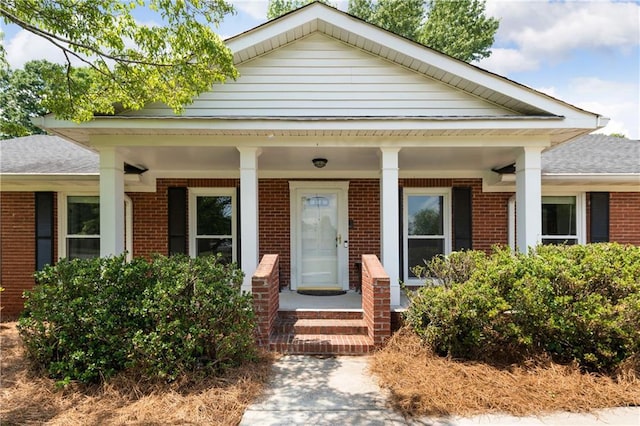 view of front facade with brick siding, roof with shingles, and a porch
