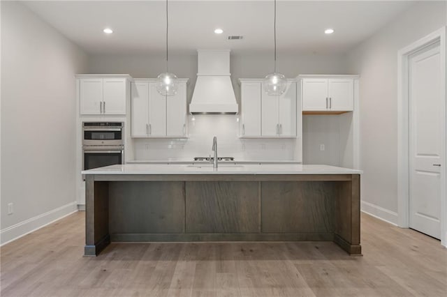 1025 Liberty Springs Dr, Woodstock, GA 30188 - kitchen with stainless steel double oven, a center island with sink, white cabinets, tasteful backsplash, and light countertops