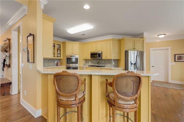 kitchen featuring appliances with stainless steel finishes, light countertops, glass insert cabinets, and a kitchen bar