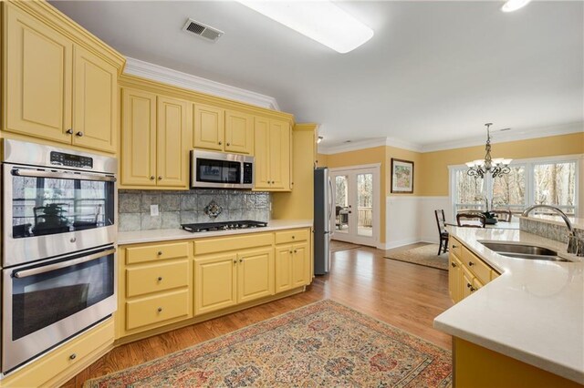 kitchen with a sink, light countertops, ornamental molding, appliances with stainless steel finishes, and plenty of natural light