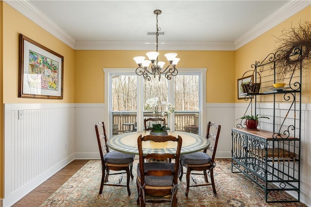 dining area with a wainscoted wall, crown molding, visible vents, wood finished floors, and a chandelier