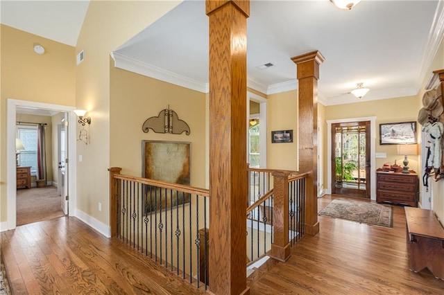 corridor with decorative columns, visible vents, ornamental molding, an upstairs landing, and wood finished floors