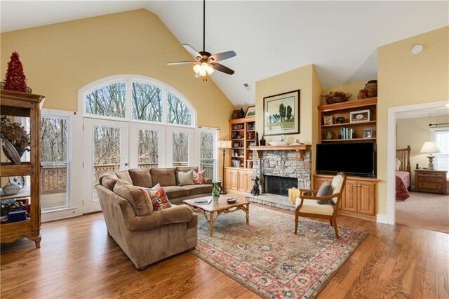 living area featuring high vaulted ceiling, light wood finished floors, a fireplace, and a healthy amount of sunlight