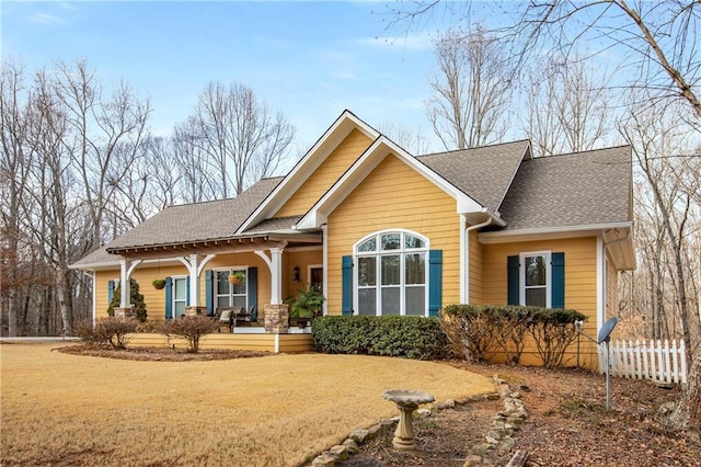 view of front of house with a porch, a front lawn, a shingled roof, and fence