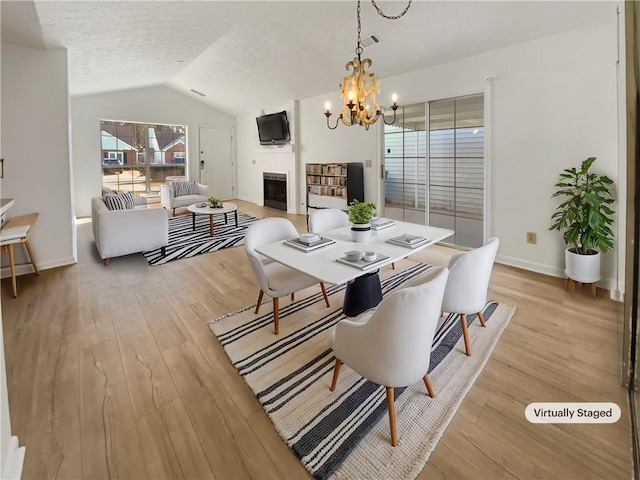 dining room featuring light wood-style flooring, a fireplace, baseboards, a chandelier, and vaulted ceiling