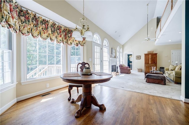 dining space with a wealth of natural light, high vaulted ceiling, wood-type flooring, and ceiling fan with notable chandelier