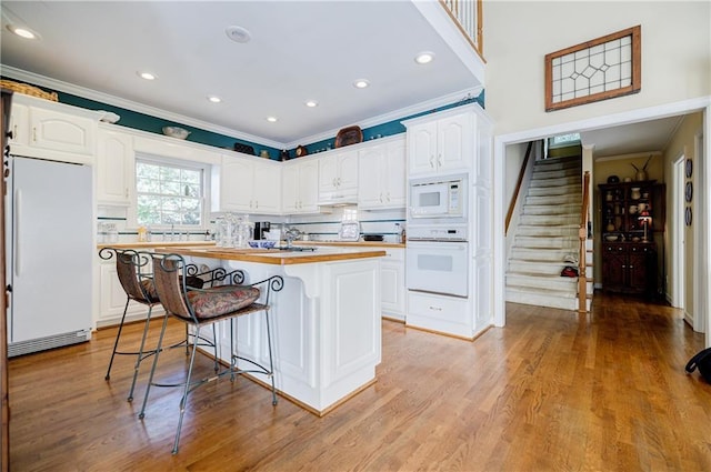 kitchen with a center island, white appliances, white cabinets, light hardwood / wood-style floors, and butcher block counters