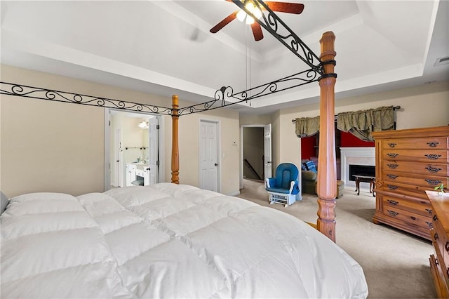 bedroom with a raised ceiling, ceiling fan, light colored carpet, and connected bathroom