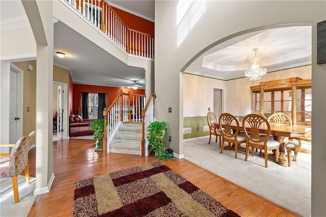 entryway featuring a raised ceiling, wood-type flooring, ceiling fan with notable chandelier, and ornamental molding