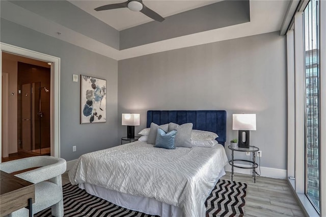 bedroom with a raised ceiling, ceiling fan, and light wood-type flooring