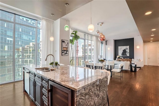 kitchen featuring dark wood-type flooring, sink, light stone counters, pendant lighting, and beverage cooler