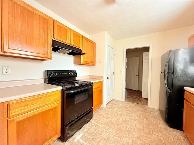 kitchen featuring baseboards, brown cabinetry, under cabinet range hood, light countertops, and black appliances