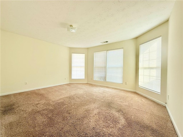 unfurnished room featuring light carpet, baseboards, visible vents, and a textured ceiling