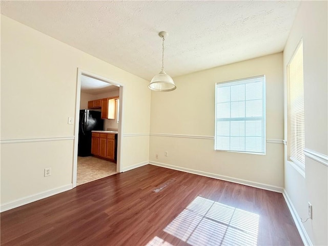 empty room featuring a textured ceiling, wood finished floors, and baseboards