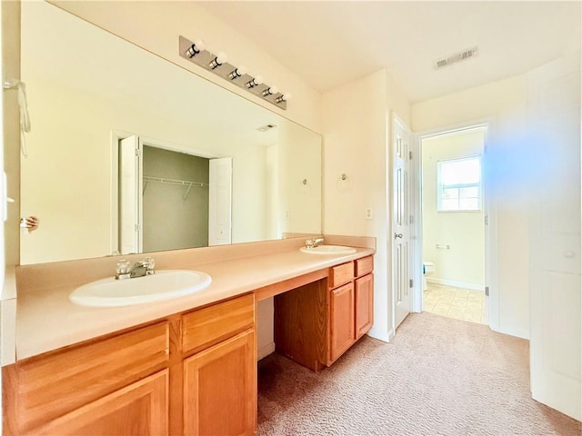 bathroom with visible vents, double vanity, a sink, and toilet