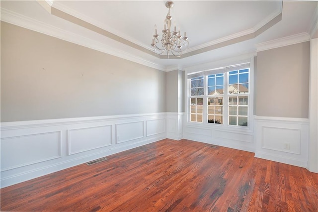 spare room featuring ornamental molding, dark hardwood / wood-style flooring, a raised ceiling, and a notable chandelier