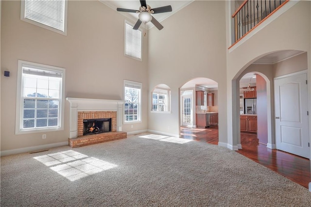 unfurnished living room with dark colored carpet, a brick fireplace, ceiling fan, and crown molding