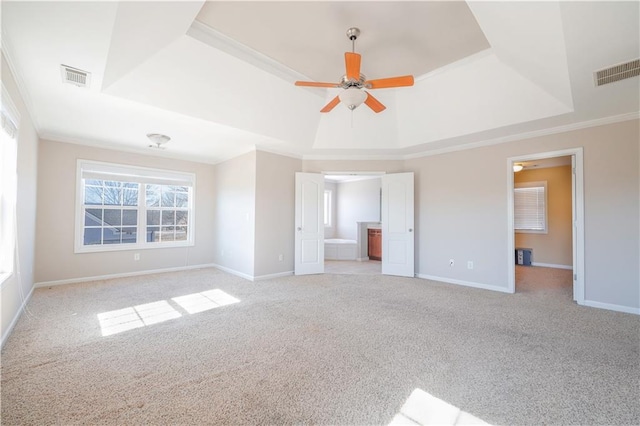 unfurnished bedroom featuring crown molding, ensuite bath, ceiling fan, a tray ceiling, and light colored carpet