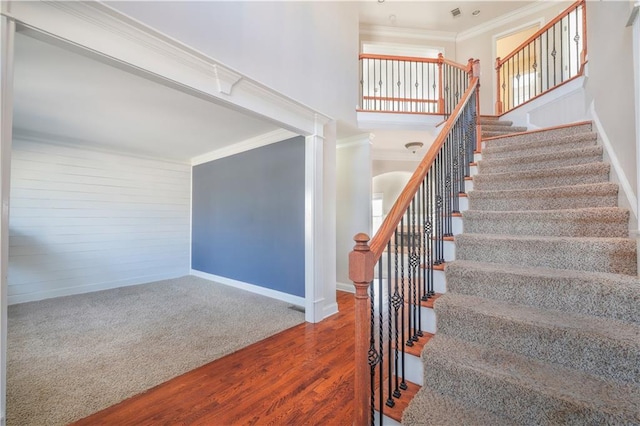 stairs featuring crown molding, a towering ceiling, and wood-type flooring