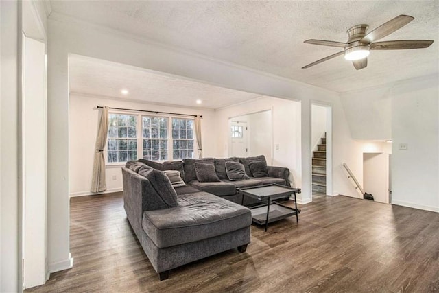 living room featuring a textured ceiling, dark wood-type flooring, baseboards, stairs, and crown molding