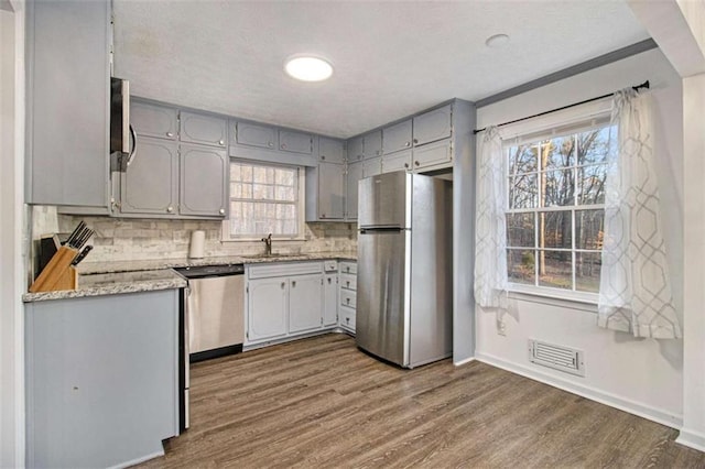 kitchen with gray cabinetry, stainless steel appliances, dark wood-type flooring, a sink, and light countertops