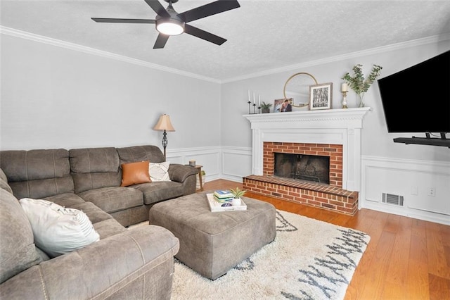 living area featuring a brick fireplace, a textured ceiling, a ceiling fan, wood finished floors, and visible vents