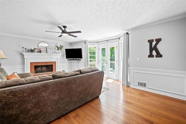 living room with ornamental molding, a ceiling fan, light wood-style flooring, and a brick fireplace