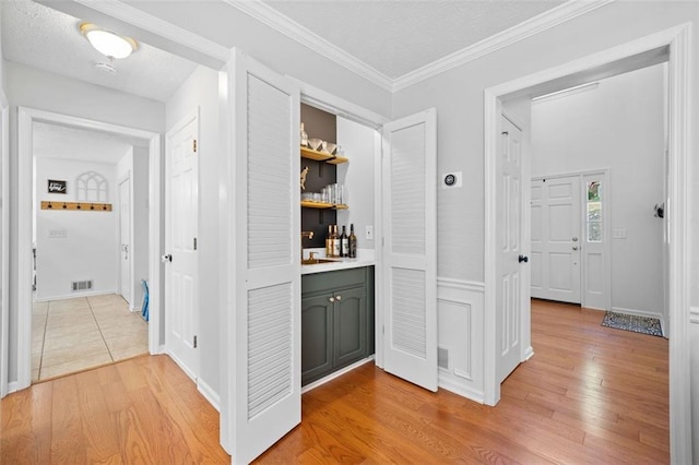 hallway with light wood-style floors, ornamental molding, a textured ceiling, and visible vents
