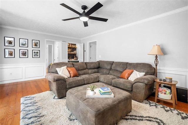 living area with ornamental molding, ceiling fan, a wainscoted wall, and hardwood / wood-style flooring