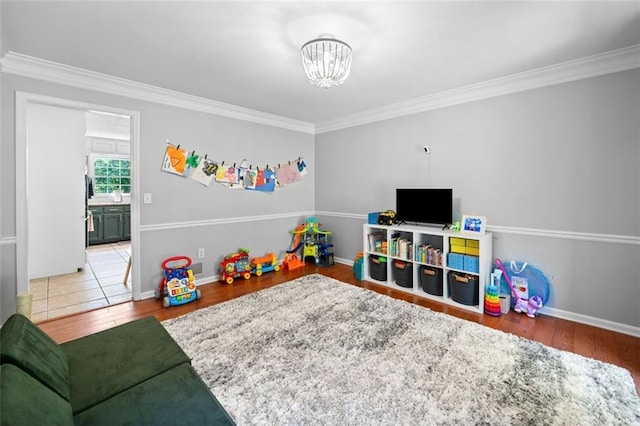 game room featuring baseboards, an inviting chandelier, ornamental molding, and wood finished floors