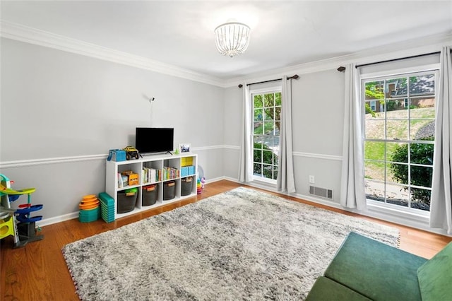 recreation room featuring crown molding, a chandelier, baseboards, wood finished floors, and visible vents